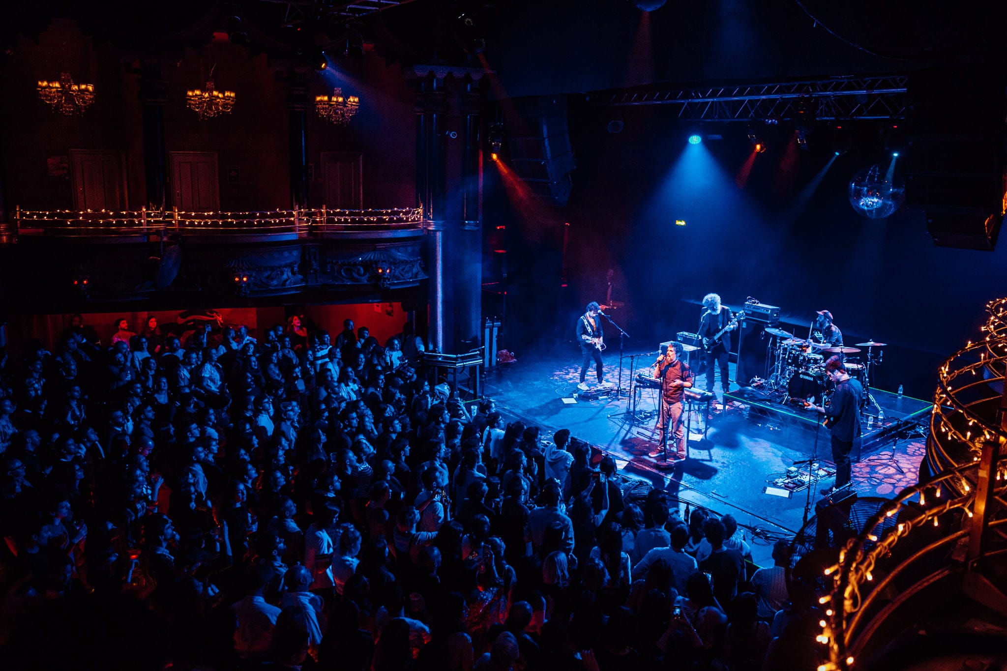 Concierto de música en vivo en sala con público y escenario iluminado.